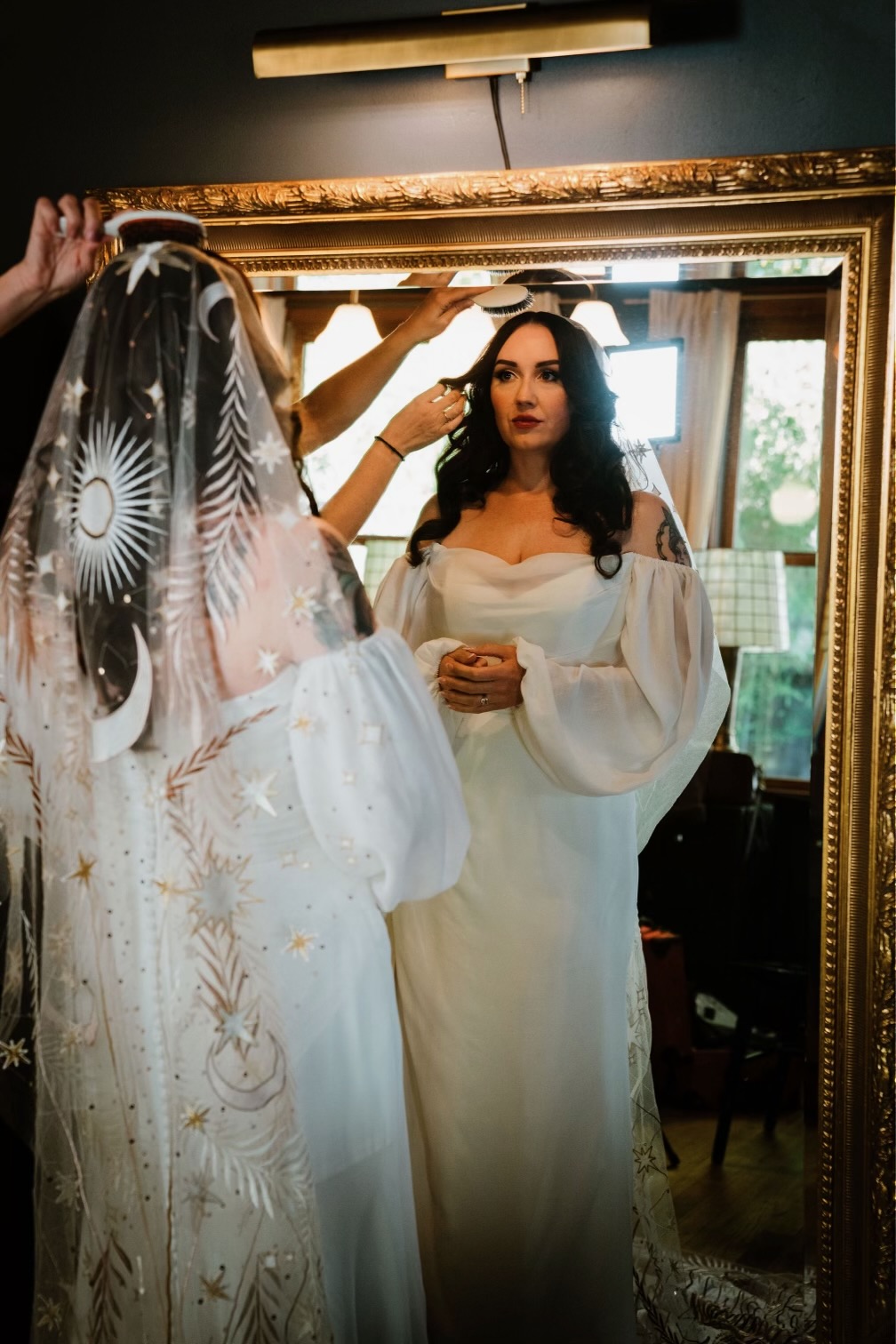A bride having her hair finished in front of an antique mirror before the ceremony